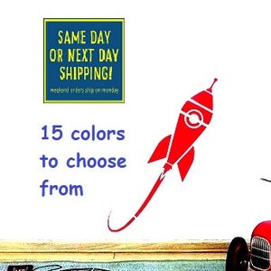 May include: Red rocket ship wall decal with a white background. The decal is available in 15 colors. The text "SAME DAY OR NEXT DAY SHIPPING!" is in a blue box with yellow text. The text "15 colors to choose from" is in blue text.