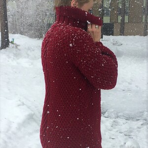 May include: A close-up of a woman wearing a red knitted turtleneck sweater. The sweater has a textured knit and is covered in small white dots, possibly snow.