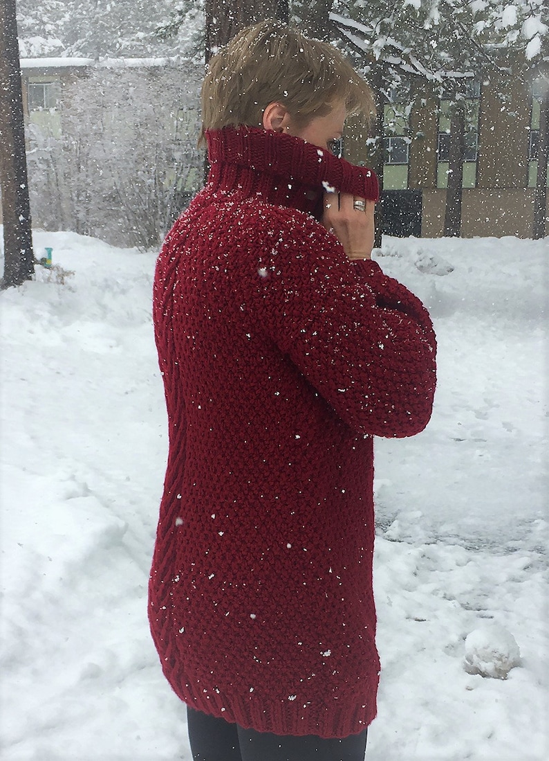 May include: A close-up of a woman wearing a red knitted turtleneck sweater. The sweater has a textured knit and is covered in small white dots, possibly snow.