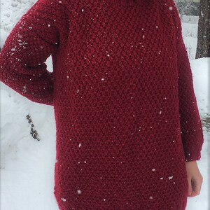 May include: A deep red knitted turtleneck sweater with a textured stitch pattern. The sweater is loose fitting and has a long, relaxed silhouette.