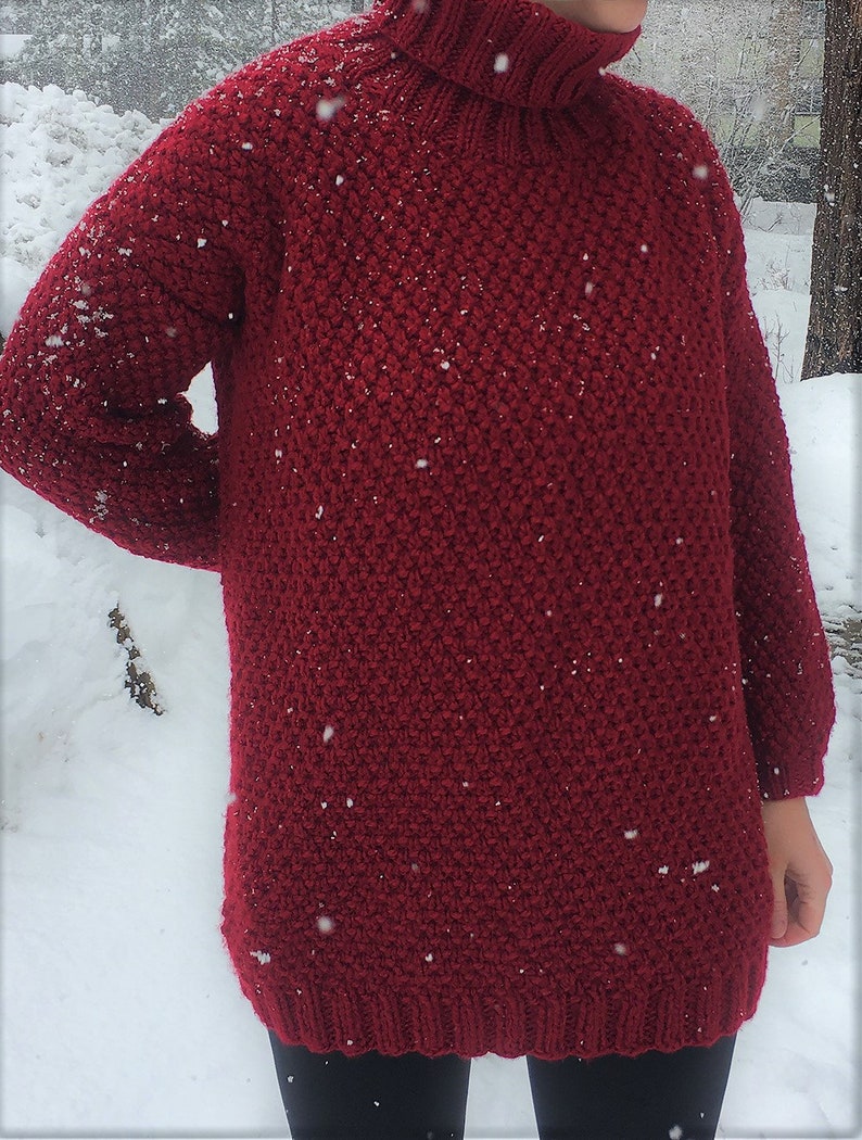 May include: A deep red knitted turtleneck sweater with a textured stitch pattern. The sweater is loose fitting and has a long, relaxed silhouette.