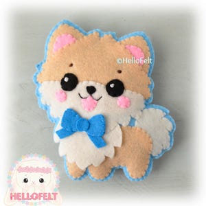 May include: A felt toy dog with a blue bow tie. The dog is brown and white with pink cheeks and black eyes. The dog is wearing a blue bow tie. The dog is sitting on a blue background. The text "@HelloFelt" is in the upper right corner of the image.