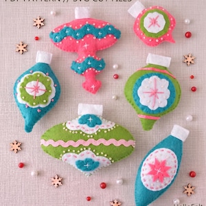 May include: A collection of handmade felt Christmas ornaments in various shapes and colors. The ornaments include pink, green, and teal designs with white and pink accents. The image also includes wooden snowflake cutouts and the text "PDF PATTERN // SVG CUT FILES".