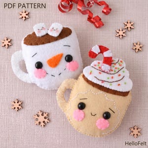 May include: Two felt coffee cup ornaments. One is white with a snowman face and marshmallows. The other is tan with whipped cream and a candy cane. The text "PDF PATTERN" is at the top.