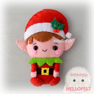 May include: A handmade felt elf doll with a red hat, white trim, and a sprig of holly. The elf has brown hair, pink ears, and a smiling face. The elf is wearing a red outfit with a green collar and a black belt with a gold buckle. The text "HelloFelt" is visible.
