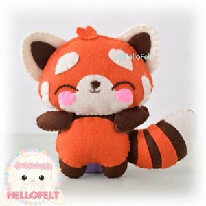 May include: A handmade felt red panda plush toy. The plush features a smiling face with pink cheeks, white accents, and brown ears, arms, and legs. The red panda has a striped tail and is made of orange, brown, and white felt. The text "HelloFelt" is visible.