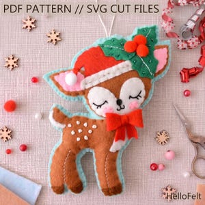 May include: A handmade felt deer ornament with a red Santa hat, a red bow, and white spots. The deer has closed eyes and pink cheeks. The ornament is decorated with green holly and red berries. Text at the top reads "PDF PATTERN // SVG CUT FILES".