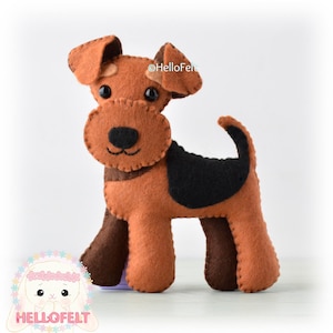 May include: A brown and black felt toy dog with a black nose and brown eyes. The dog is standing on a white surface. The text "HelloFelt" is visible in the image.