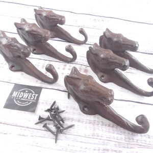 May include: Six cast iron horse head hooks in a rustic brown finish. The hooks are designed with a detailed horse head and a curved hook. Includes a small pile of screws and a label that says "MIDWEST CRAFT MARKET".