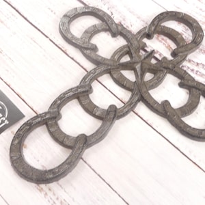 May include: A rustic, metal cross made of interlocking horseshoe shapes. The cross is a dark, weathered gray color, and rests on a white-washed wooden surface. A small card with the text "MIDWEST" is in the lower left corner.