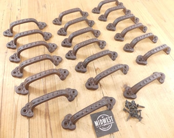 May include: A collection of sixteen dark brown cast iron drawer pulls, each featuring a textured surface with a series of raised dots along the handle and decorative clover-shaped ends. A small black square card with the text MIDWEST CRAFT HOUSE is included with a small pile of matching black metal screws.