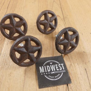May include: Four rustic, star-shaped cabinet knobs with a distressed, brown finish. The knobs are made of cast iron and have a five-point star design. A black tag with the text "MIDWEST CRAFT HOUSE" is also present.