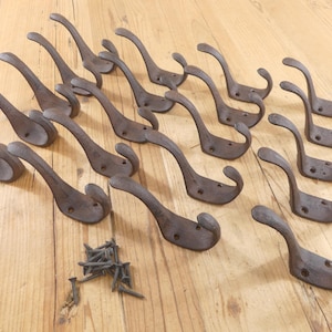 May include: A collection of antique-style, cast iron coat hooks in a rustic brown finish. Each hook has a curved design with a double hook feature and mounting holes. A small pile of screws is included.