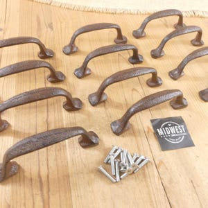 May include: A collection of ten dark brown, textured cast iron drawer pulls with curved handles and rectangular mounting bases. A small pile of silver-colored metal screws is included, along with a black square label featuring the text MIDWEST.