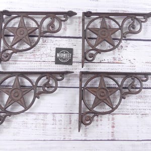 May include: Four cast iron shelf brackets with a rustic brown finish. Each bracket features a five-pointed star within a circular frame, with decorative scrollwork. The brackets are designed for wall mounting and add a vintage touch to any space.