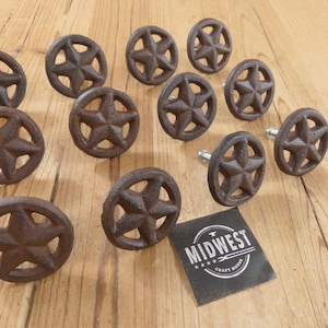 May include: A collection of rustic, brown cast iron star-shaped cabinet knobs. The knobs feature a five-pointed star design within a circular frame. A small black tag with the text "MIDWEST CRAFT HOUSE" is also present.