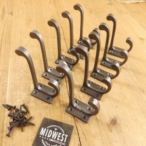 May include: Set of ten dark gray, wrought iron coat hooks with a curved design. Includes mounting screws and a Midwest Craft House label. The hooks are approximately 6 inches tall.