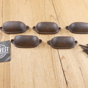 May include: Five rustic, brown cast iron drawer pulls with a textured finish, each with two mounting holes. A small pile of screws is next to the pulls. A black and white tag with the text "MIDWEST CRAFT HOUSE" is also present.