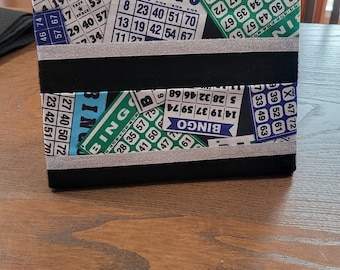 Può includere: Un pannello rivestito in tessuto nero con due file di carte da bingo colorate. Le carte hanno numeri e la parola "BINGO" stampata su di esse. Le carte sono disposte in modo casuale.