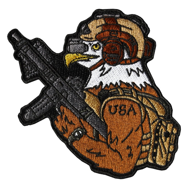 May include: Embroidered patch featuring a brown eagle wearing a helmet and holding a black rifle. The eagle has a white chest with a lightning bolt design and the word "USA" is visible on its arm.