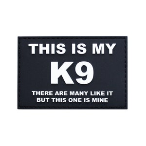 May include: Black rectangular patch with white text that reads "THIS IS MY K9". Below the large "K9" are the words "THERE ARE MANY LIKE IT BUT THIS ONE IS MINE". The patch has a black border.
