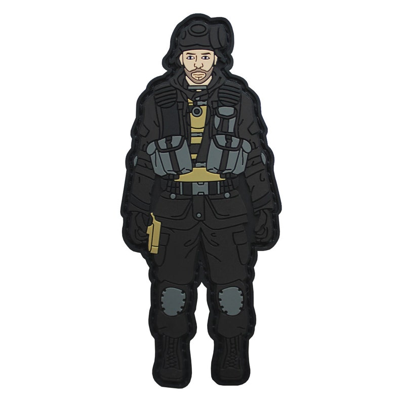 K&ouml;nnte beinhalten: Schwarzer und grauer gestickter Aufn&auml;her einer Person, die eine schwarze taktische Weste, eine schwarze Hose und einen schwarzen Hut tr&auml;gt. Die Person h&auml;lt eine Waffe in der rechten Hand.