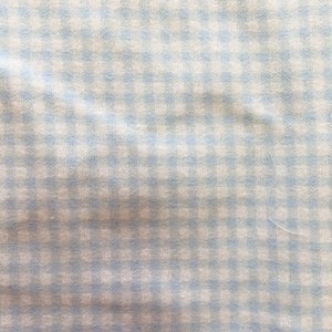 May include: A white fabric with a light blue gingham pattern. The fabric has a slightly wrinkled texture.