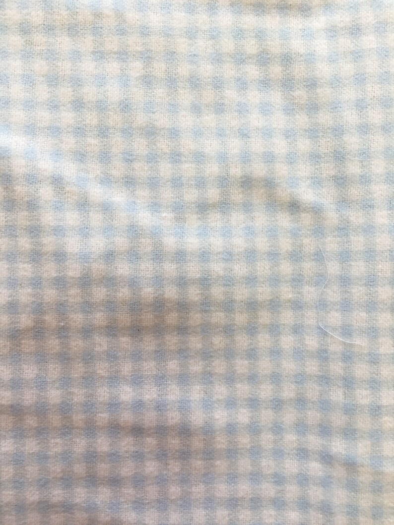 May include: A white fabric with a light blue gingham pattern. The fabric has a slightly wrinkled texture.