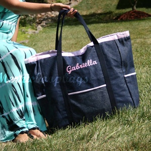 May include: A large denim tote bag with a pink trim and the name "Gabriella" embroidered on the front. The bag has multiple pockets and is perfect for carrying a variety of items.