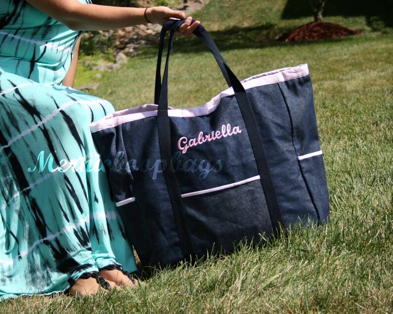 May include: A large denim tote bag with a pink trim and the name "Gabriella" embroidered on the front. The bag has multiple pockets and is perfect for carrying a variety of items.