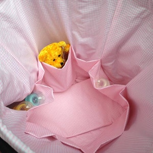 May include: A pink and white gingham diaper bag with multiple pockets and a yellow stuffed animal inside.
