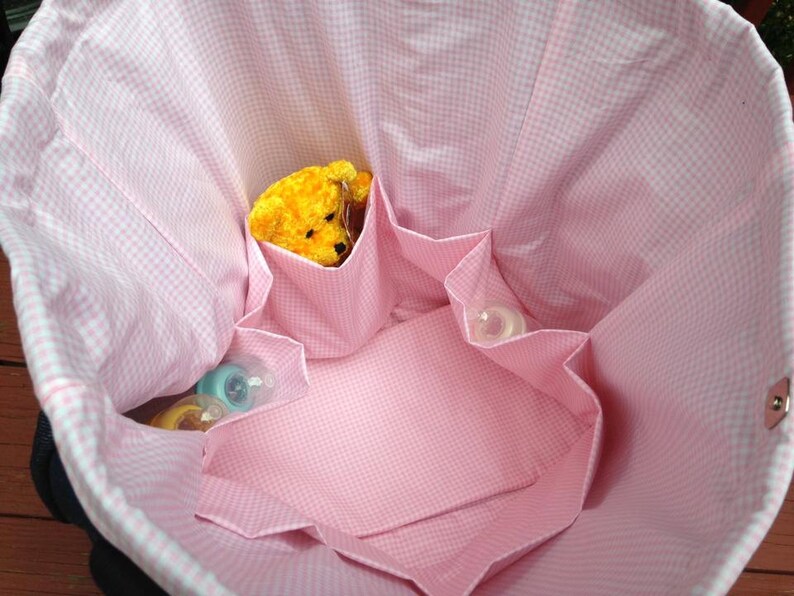 May include: A pink and white gingham diaper bag with multiple pockets and a yellow stuffed animal inside.