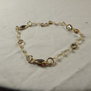 May include: A gold chain bracelet with white and dark red gemstone accents.