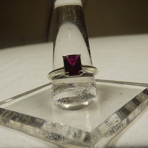 May include: A silver ring with a square-shaped, deep purple gemstone.