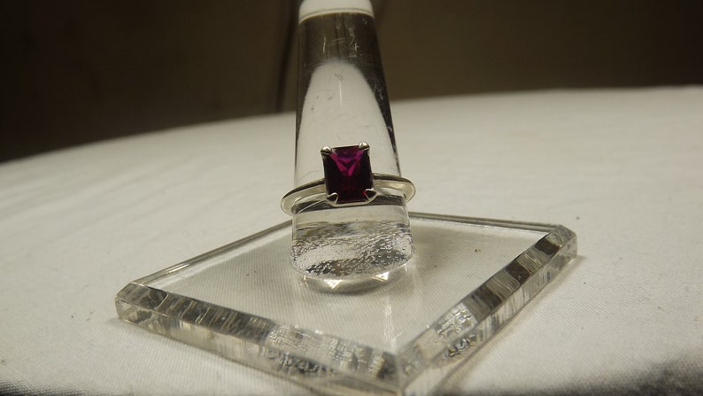May include: A silver ring with a square-shaped, deep purple gemstone.