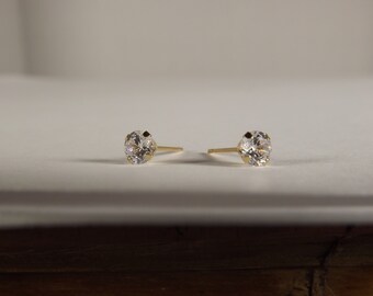 May include: A pair of gold stud earrings with clear round cubic zirconia stones.