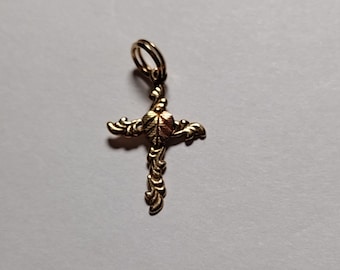 Pode incluir: Um pingente de cruz dourado com um design detalhado e ornamentado. O centro da cruz apresenta um pequeno design redondo em forma de folha.