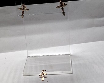 Pode incluir: Um par de brincos de cruz de ouro em um expositor de acrílico transparente.