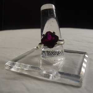 May include: A silver ring with a large, faceted, dark purple gemstone set in a prong setting.