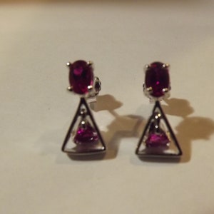 May include: A pair of silver earrings with a triangular design and red gemstones.