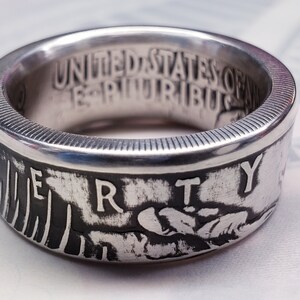 May include: Silver ring made from a United States coin. The ring features the words "United States of America" and "E Pluribus Unum" on the inside of the band. The outside of the band features the word "Liberty" and a design of an eagle's head.