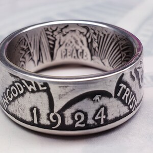 May include: A silver ring made from a 1924 Peace Dollar coin. The ring features the inscription "In God We Trust" and the year "1924".