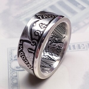 May include: A silver ring made from a 1924 Peace Dollar coin. The ring features the inscription "IN GOD WE TRUST" and "PEACE" on the side. The ring is made from a real coin and is a unique piece of jewelry.