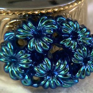 May include: A close-up of a blue iridescent floral design. The design is made of metal and has a shiny finish.