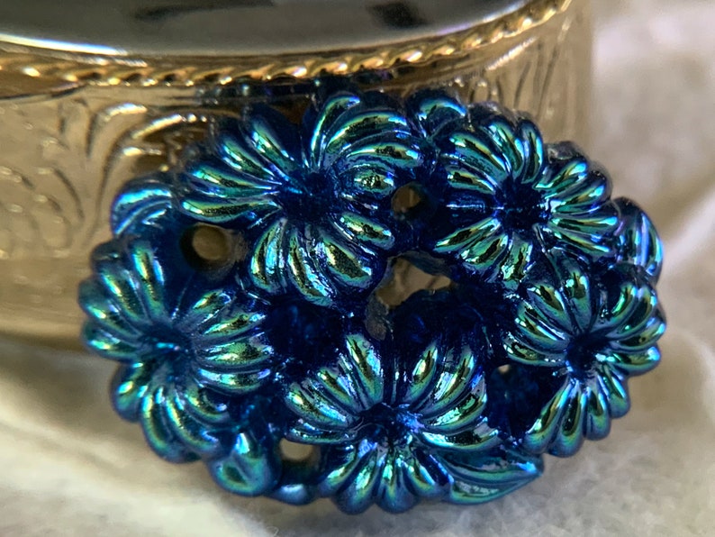 May include: A close-up of a blue iridescent floral design. The design is made of metal and has a shiny finish.