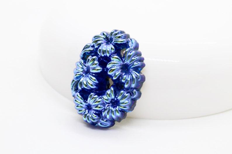 May include: A cluster of blue iridescent flowers in an oval shape. The flowers are made of metal and have a textured surface.