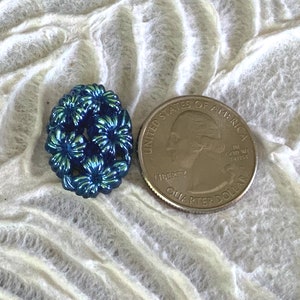 May include: A blue iridescent button with a floral design. The button is about the size of a US quarter.