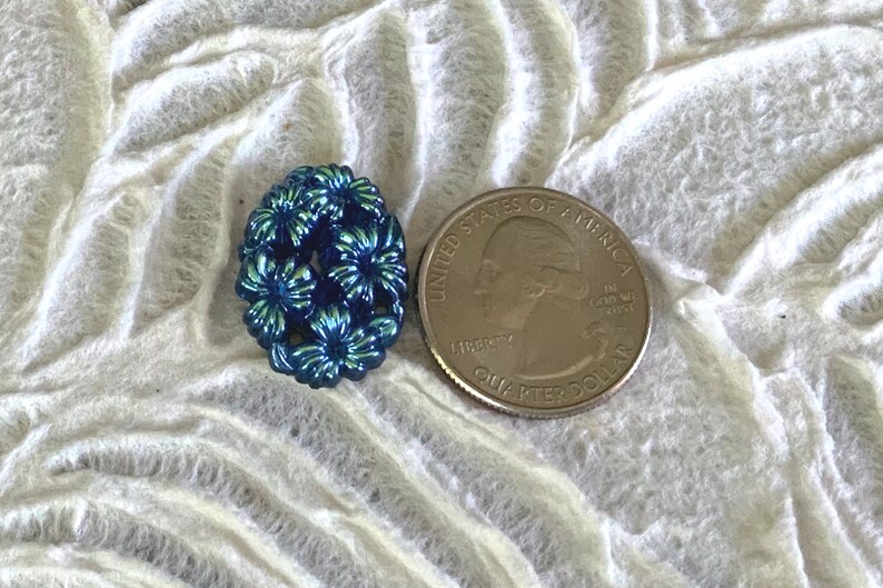 May include: A blue iridescent button with a floral design. The button is about the size of a US quarter.