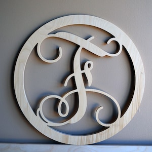 May include: A wooden letter "F" in a circular frame. The letter is in a cursive script style, with decorative swirls. The wood has a natural, light color. The frame is also made of wood and is circular.