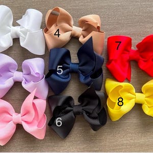 May include: Eight different colored hair bows with numbers 1 through 8 on them. The bows are made of a soft, textured fabric and are arranged in a row.